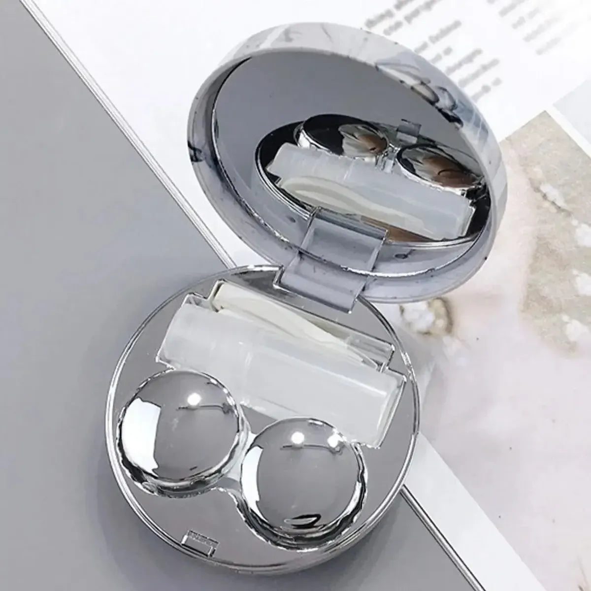Estuche de mármol plateado abierto con espejo, contenedor de lentes y recipiente para solución